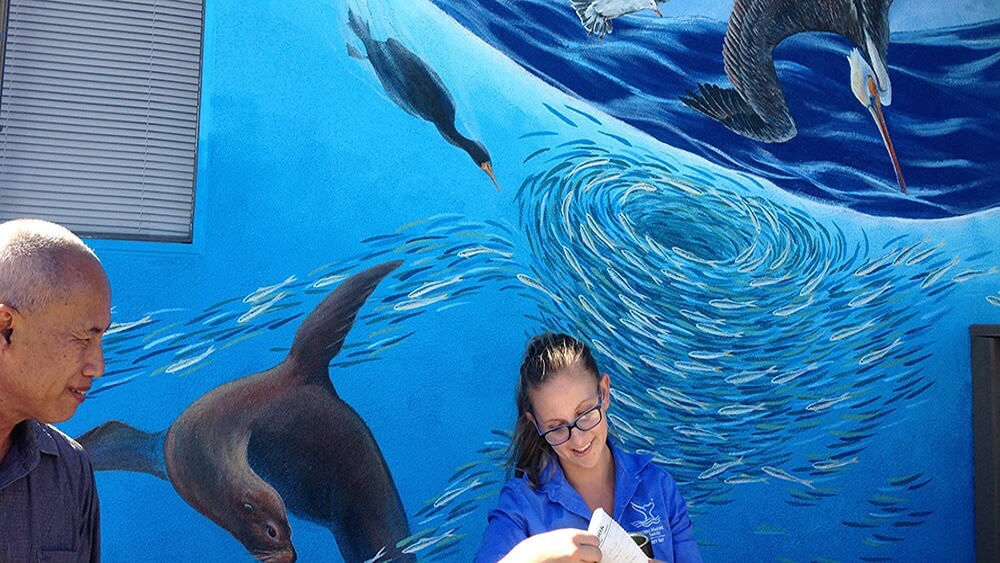 A blue mural of water and animals, with two people standing in front.